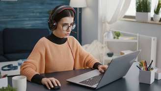 Young woman attending video call meeting on laptop with headphones, talking on remote teleconference for school class work. Female student using headset and computer on videoconference.