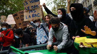 Manifestantes exibem cartazes atrás de uma barricada em Paris, no dia 7 de outubro de 2026