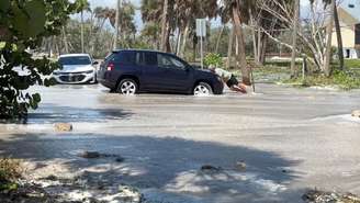 Um homem tenta empurrar um carro enquanto ondas invadem a estrada antes da chegada do furacão Isaias, em Englewood, Flórida (EUA), em 9 de outubro de 2026.