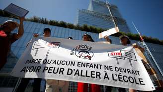 Manifestantes exibem faixa com a frase “Nenhuma criança deveria ter medo de ir à escola” durante ato em frente ao Tribunal Criminal de Paris, em 26 de maio de 2026, na véspera do início do julgamento de um monitor escolar acusado de violência contra alunos da educação infantil.