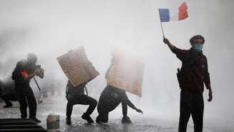 Manifestante mascarado segura bandeira francesa durante protestos de estudantes e confrontos com forças de ordem, em Paris, em 13 de outubro de 2026.