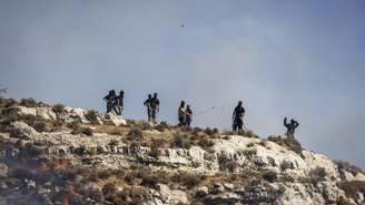Foto de colonos israelenses encapuzados lançando pedras contra palestinos em Sinjil, em 4 de julho de 2025, ilustra a tensão na Cisjordânia ocupada.