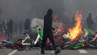 Um manifestante mascarado passa por bicicletas em chamas durante confrontos em uma rua de Paris, em meio a um dia de manifestações contra o custo de vida e o aumento dos preços dos combustíveis, na França, em 17 de outubro de 2026.