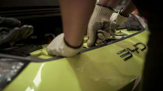 Close em um carro BYD amarelo com o capô aberto e mãos de luvas mexendo em seu interior
