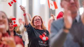Participantes reagem durante um evento noturno do Forever Canadian sobre o referendo em Edmonton, Alberta, Canadá, na segunda-feira, 19 de outubro de 2026. Uma mulher ruiva segura uma bandeira do Canadá.
