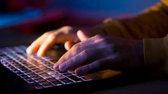 Mão em teclado de laptop, em ambiente escuro