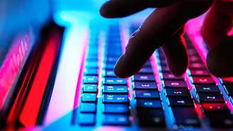 Uma imagem de arquivo mostrando um laptop com algumas mãos digitando em teclas com iluminação neon.