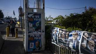 Colonos israelenses aguardam perto de posto de segurança decorado com cartazes eleitorais em Gush Etzion, na Cisjordânia ocupada, às vésperas das eleições legislativas.