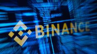 O logotipo da Binance em contraste com um texto azul desfocado, típico de computador.