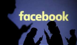 Pessoas utilizam celulares diante de projeção do logo do Facebook
