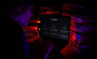 Um homem usando o computador na aba do ChatGPT. Ele está no escuro