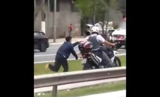 Homem apresenta dificuldade ao andar enquanto está algemado a moto conduzida por policial; cena tem gerado revolta nas redes sociais