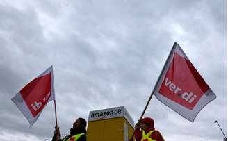 <p>Membros do sindicato Verdi com bandeiras do lado de fora de um armazém da Amazon</p>