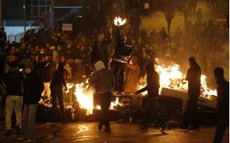 <p>Manifestantes contra o governo se protegem das forças policias atrás e barricadas durante protesto em Ankara, na noite de 12 de março</p>