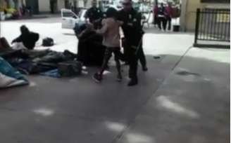 Vídeo feito por um observador mostra pelo menos quatro policiais lutando com o homem no solo ao lado do que parece ser uma série de lonas de plástico e sacos de dormir na calçada