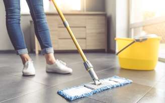 Pessoa limpando o piso com um rodo e uma balde
