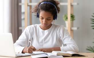 Menina negra estudando com fones de ouvido e computador