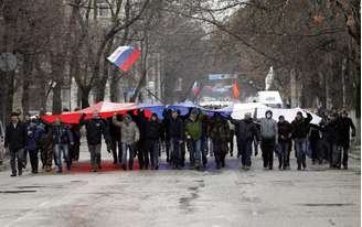 <p>Segurando uma bandeira russa, manifestantes marcham em frente ao prédio do governo, na Crimeia. De acordo com o Ministro do Interior ucraniano, a polícia está em alerta máximo depois que dezenas de manifestantes invadiram o edifício do Parlamento de Simferopol</p>