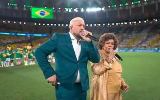 Belo e Alcione cantam o hino nacional brasileiro durante jogo do Brasil no Maracanã.