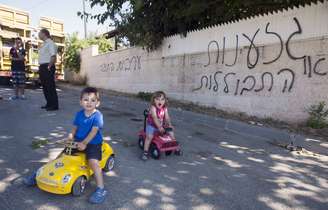 <p>Crianças brincam em frente ao muro pichado com as palavras "árabes fora" e "racismo ou assimilação", no povoado árabe israelense de Abu Ghosh, em 18 de junho</p>