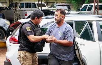 Homem com algemas na mão sendo retirado de carro por policial