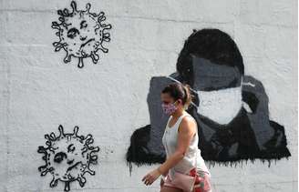 Mulher passa por grafite do presidente Jair Bolsonaro ajustando sua máscara protetora e em forma de vírus, em meio ao surto de Covid-19 no Rio de Janeiro. 02/07/2020. REUTERS/Sergio Moraes