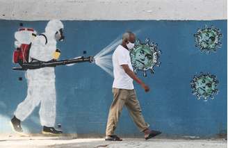 Homem passa pela frente de um grafite, enquanto um funcionário do serviço de saúde borrifa um spray contra o coronavírus. 12/6/2020. REUTERS/Sergio Moraes