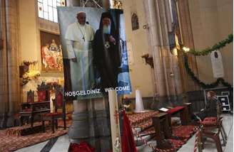 <p>Mulher reza perto de cartaz com fotos do Papa Francisco e do patricarca Bartolomeu em igreja católica no centro de Istambul</p>