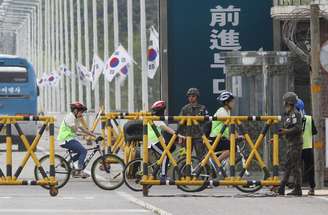 Estudantes passam de bicicleta por guardas em uma ponte em Paju, na Coreia do Sul