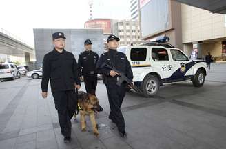 Policiais armados fazem patrulha com cão ao longo de uma área de negócios em Pequim nesta segunda-feira. A China reforçou a segurança na capital pela violência