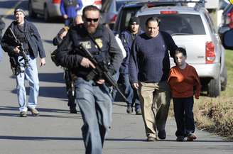 Policiais armados caminham em meio a pais que levam seus filhos embora da escola Sandy Hook