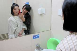<p>Xu Jianmei se olha no espelho ao lado da mãe após ter a face reconstruída: cirurgia foi bem sucedida</p>