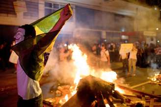 Manifestante abre a bandeira do Brasil em frente a fogueira durante confronto com a polícia, em Niterói