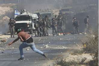 <p>Manifestante palestino joga pedras em direção a soldados israelenses durante confrontos em um protesto contra a ofensiva israelense em Gaza, na Cisjordânia, em 8 de agosto</p><p> </p>