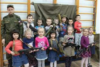 Crianças de um jardim de infância de São Petesburgo, na Rússia, posam com armas ao lado de um militar