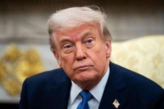 Presidente americano Donald Trump, de terno, olhando para a câmera