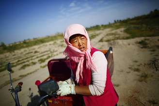<p>Mulher descansa sob forte calor após trabalhar colhendo algodão próximo a rio que secou na China</p>