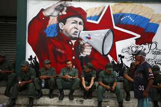 Soldados venezuelanos sentam em frente a um mural com a imagem de Hugo Chávez, em 27 de fevereiro