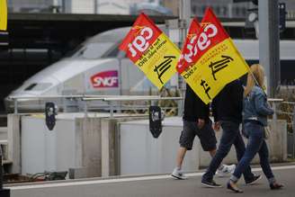 <p>Trabalhadores ferroviários seguram bandeiras de protesto ao passar em frente a uma estação ferroviária de Nantes, a oeste da França</p>