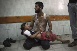 <p>Palestino segura no colo uma criança que foi ferida durante um bombardeio israelense a uma escola, no norte da Faixa de Gaza</p>