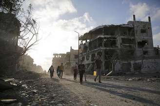<p>Palestinos caminham diante de prédios destruídos na Cidade de Gaza, em 6 de agosto</p>