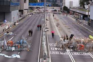 <p>Pedestres passam por obstáculos e barricadas colocadas por manifestantes em avenida de Hong Kong</p>