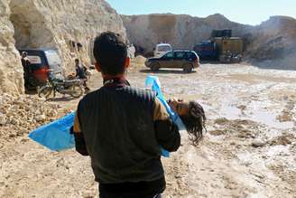Homem carrega corpo de criança que teria morrido durante bombardeio com armas químicas na Síria