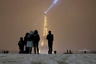 Turistas observam de longe a torre Eiffel cercados pela neve