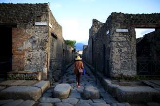 Turista caminha ao longo de uma antiga rua de paralelepípedos romanos em Pompéia, Património Mundial da UNESCO