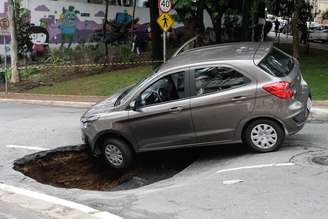 Um veículo caiu no buraco que se abriu após o asfalto ceder na Rua Carlos Comenale, no bairro da Bela Vista.