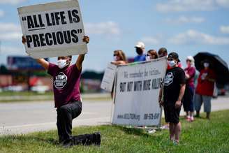 O reverendo Sylvester Edwards, presidente do Terre Haute NAACP, se ajoelha enquanto outros manifestantes seguram cartazes perto do Complexo Correcional Federal, Terre Haute, para mostrar sua oposição à pena de morte e execução de Daniel Lewis Lee, que é condenado pelo assassinato de três membros de uma família do Arkansas em 1996, e seria a primeira execução federal em 17 anos, em Terre Haute, Indiana, nos Estados Unidos. 13/07/2020. REUTERS/Bryan Woolston.