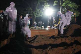 Coveiros com trajes de proteção fazem o sepultamento noturno no cemitério de Vila Formosa, em São Paulo