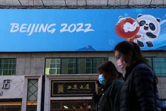 Pessoas caminham próximo a cartaz com o logo da Olimpíada de Inverno Pequim 2022 em Pequim
27/10/2021 REUTERS/Tingshu Wang