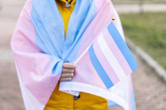 Transgender woman covered with the transgender flag and holding a flag in the hand for defending her rights